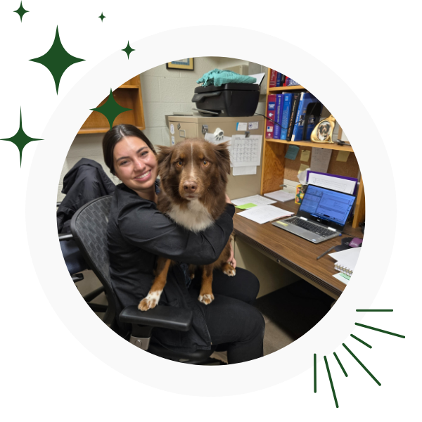 A woman holds a dog while sitting in front of a computer