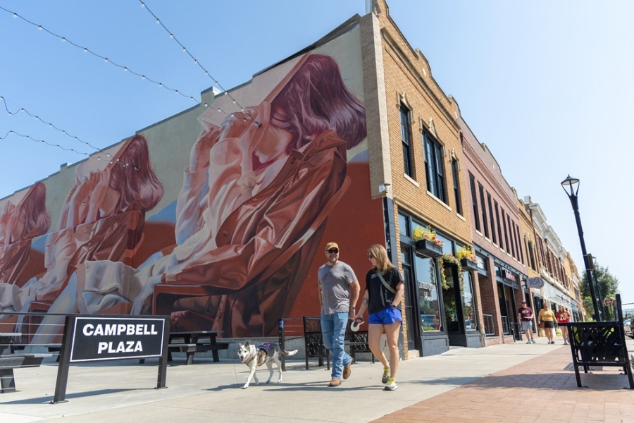 A couple walks their dog in front of a colorful mural